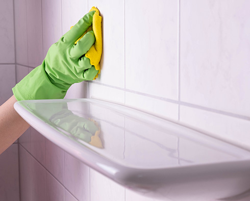 Hand Holding Towel Wiping Shower Tiles and Grout Using Chlorine Which Regular Use May Deteriorate Grout
