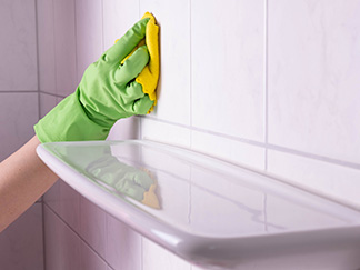 Hand Holding Towel Wiping Shower Tiles and Grout Using Chlorine Which Regular Use May Deteriorate Grout